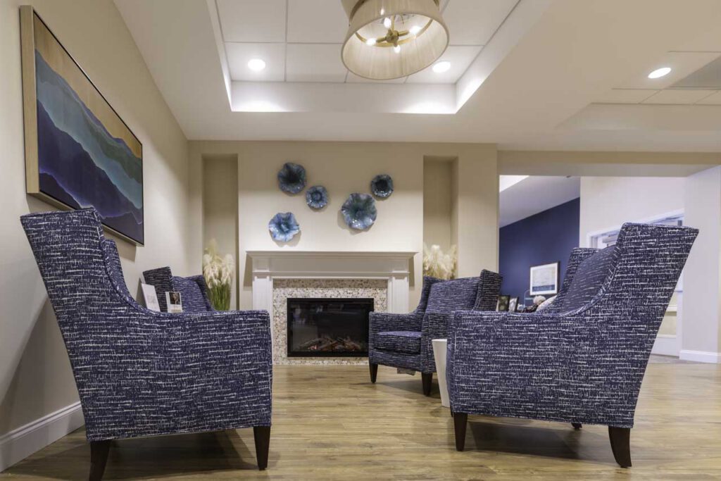 A cozy lounge with four blue patterned armchairs arranged around a fireplace, modern art on the walls, and a wooden floor, creating a warm and inviting atmosphere.